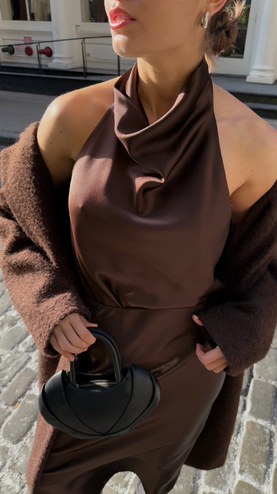 Chocolate satin halter, textured coat off the shoulders and the sculpted black top-handle bag