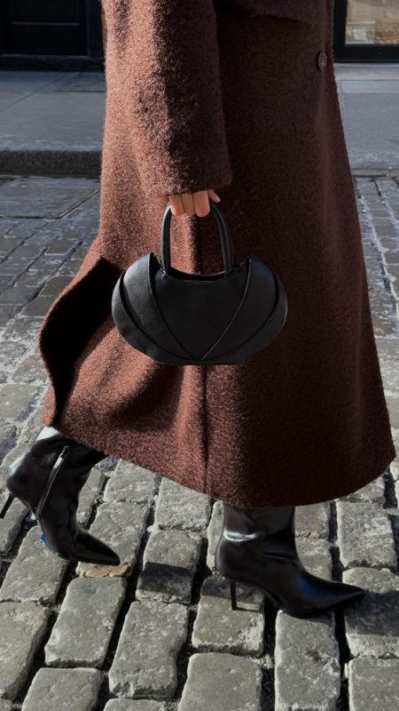 Detail of the sculpted top-handle bag against the brown coat
