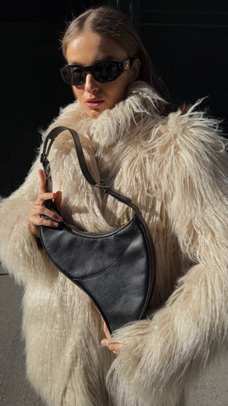 Cream faux-fur coat and the black crescent bag against a dark doorway