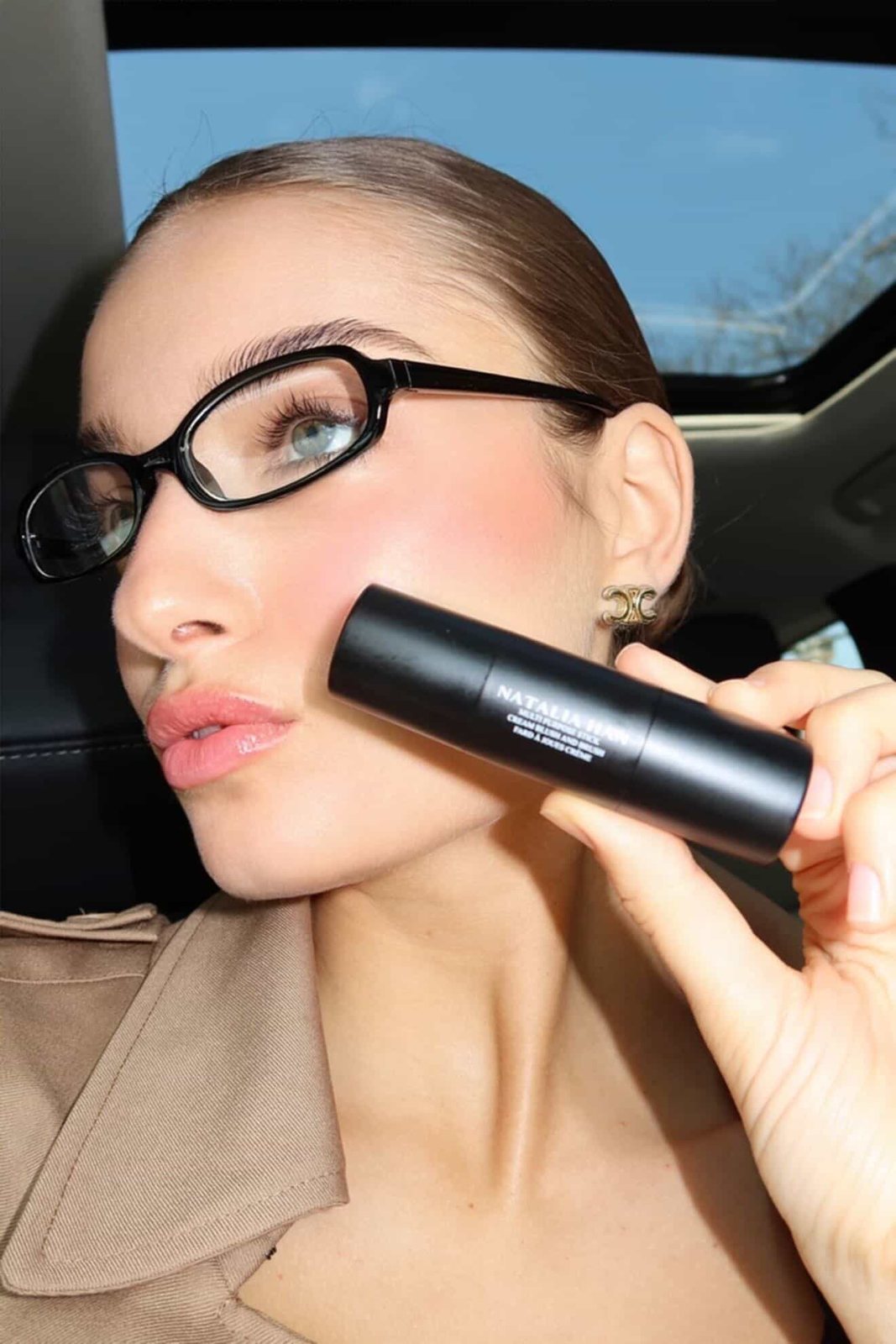Model in black glasses pressing the Natalia Han Beauty blush stick to her cheek in a car