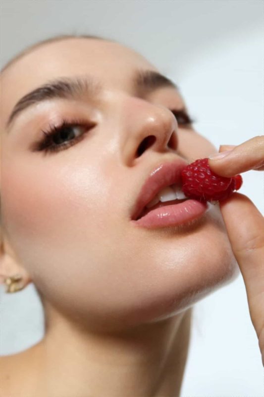 Beauty close-up of glossy lips biting a raspberry