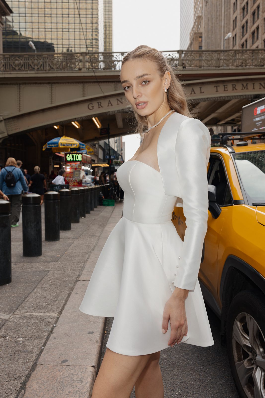 Model in a Sienricher bridal mini and bolero beside a yellow taxi outside Grand Central Terminal