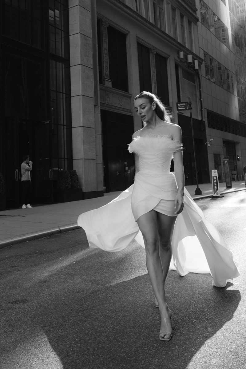 Model in a Sienricher feathered bridal mini dress with a flowing train, walking a Manhattan street
